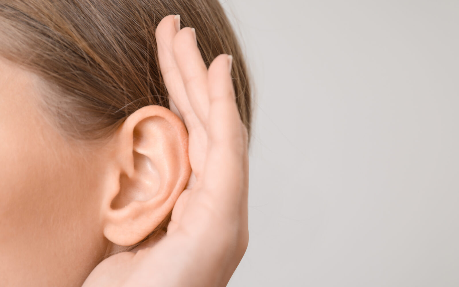 Young woman with hearing problem on light background, closeup