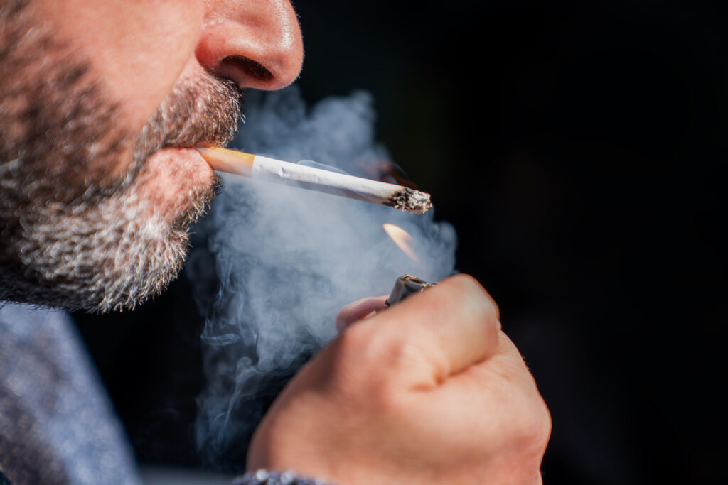 Close up of bearded man holding a lighter and smoking a cigarette on black background