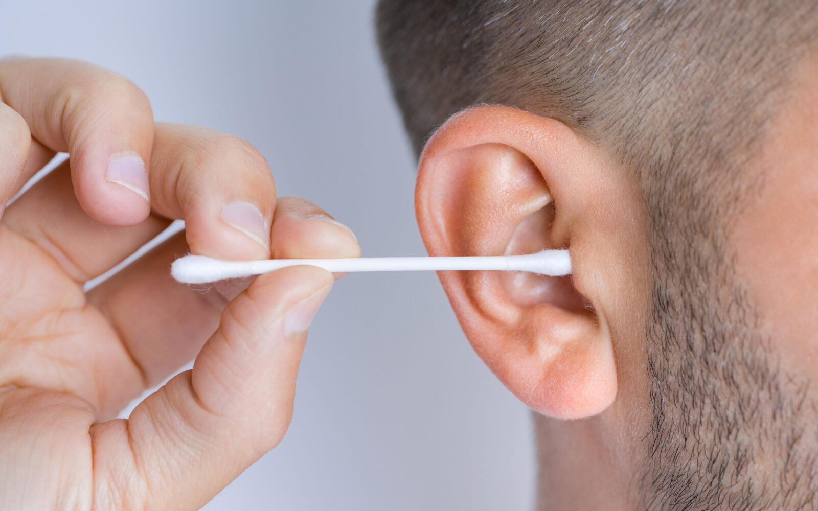 Closeup of man cleaning dirty ears with cotton swab or cotton stick Ear cleaning and ear care