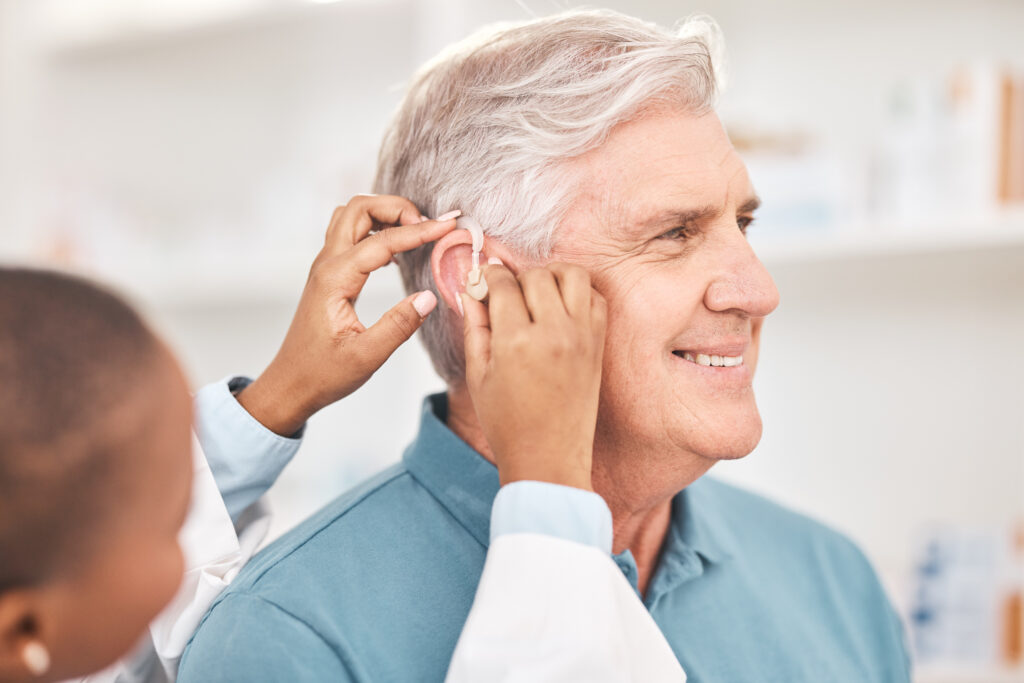 Helping, man and doctor with hearing aid, technology or healthcare or medical device consultation for deaf patient with tinnitus Listening, test and exam ear tech with nurse or senior male in clinic