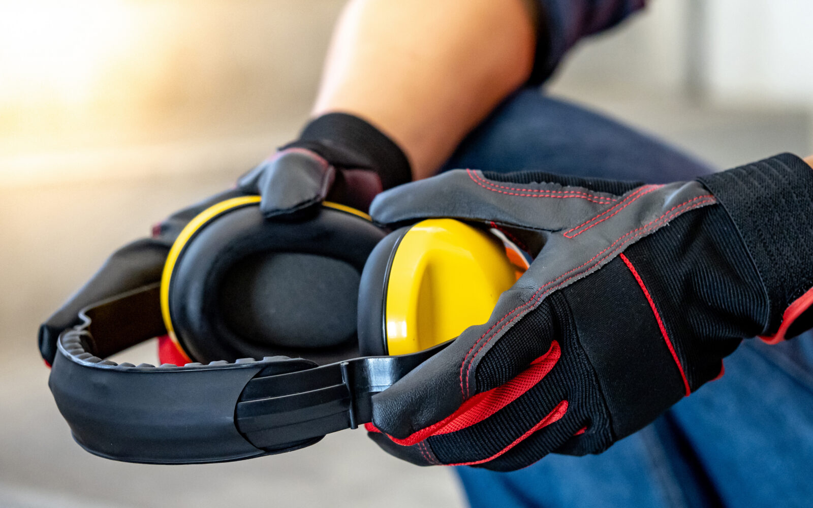 Male worker hand with black and red protective gloves holding yellow safety ear muffs or ear protectors preparing to wear on his head Equipment for high noise reduction