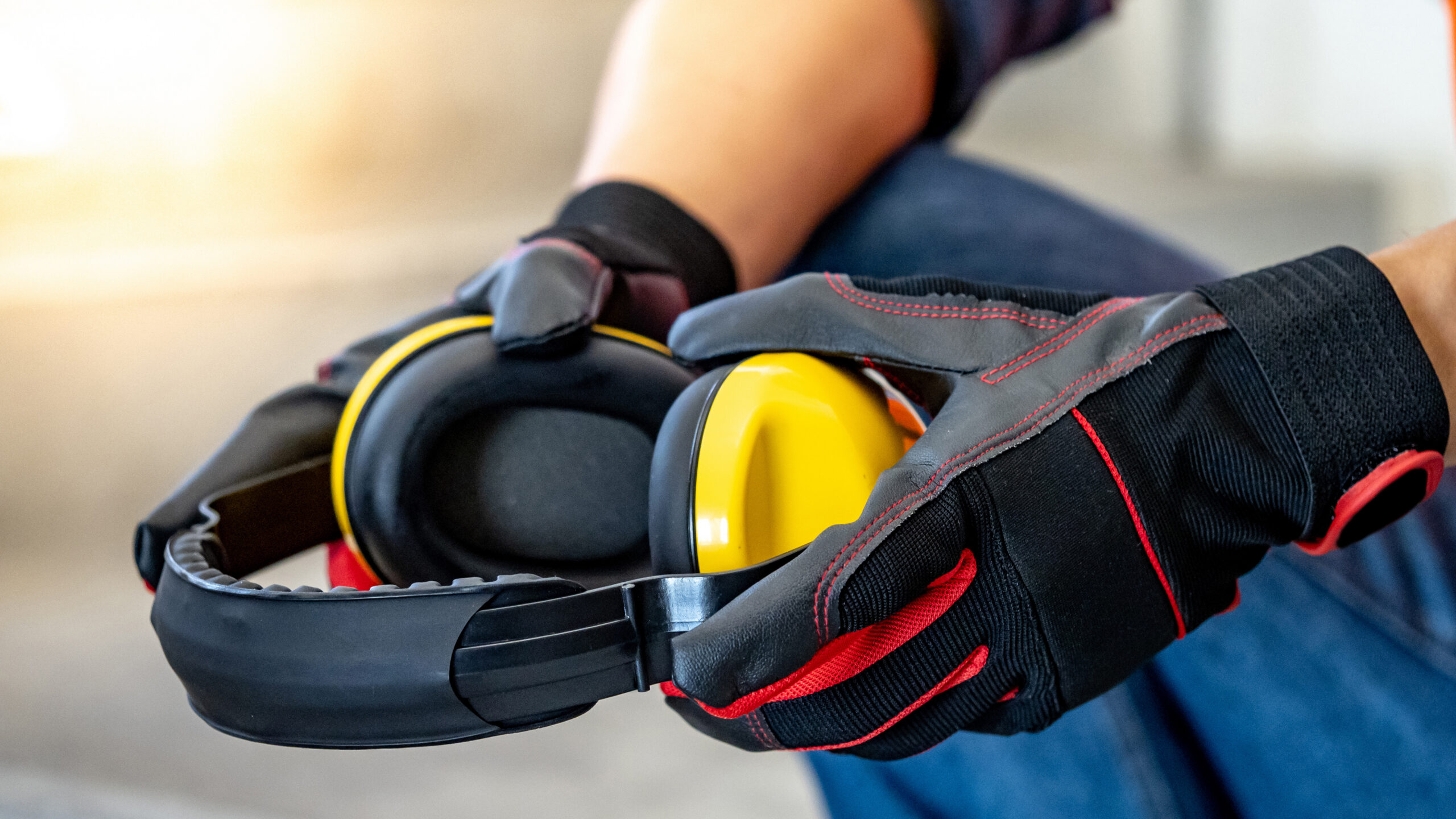 Male worker hand with black and red protective gloves holding yellow safety ear muffs or ear protectors preparing to wear on his head Equipment for high noise reduction