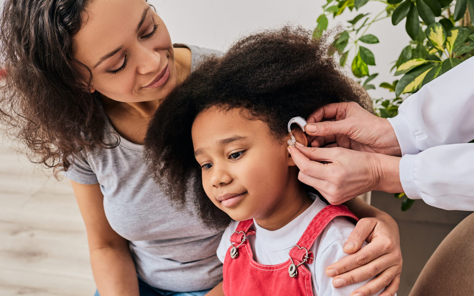 Hearing treatment for a child African American girl with her mother during installation hearing aid by her audiologist