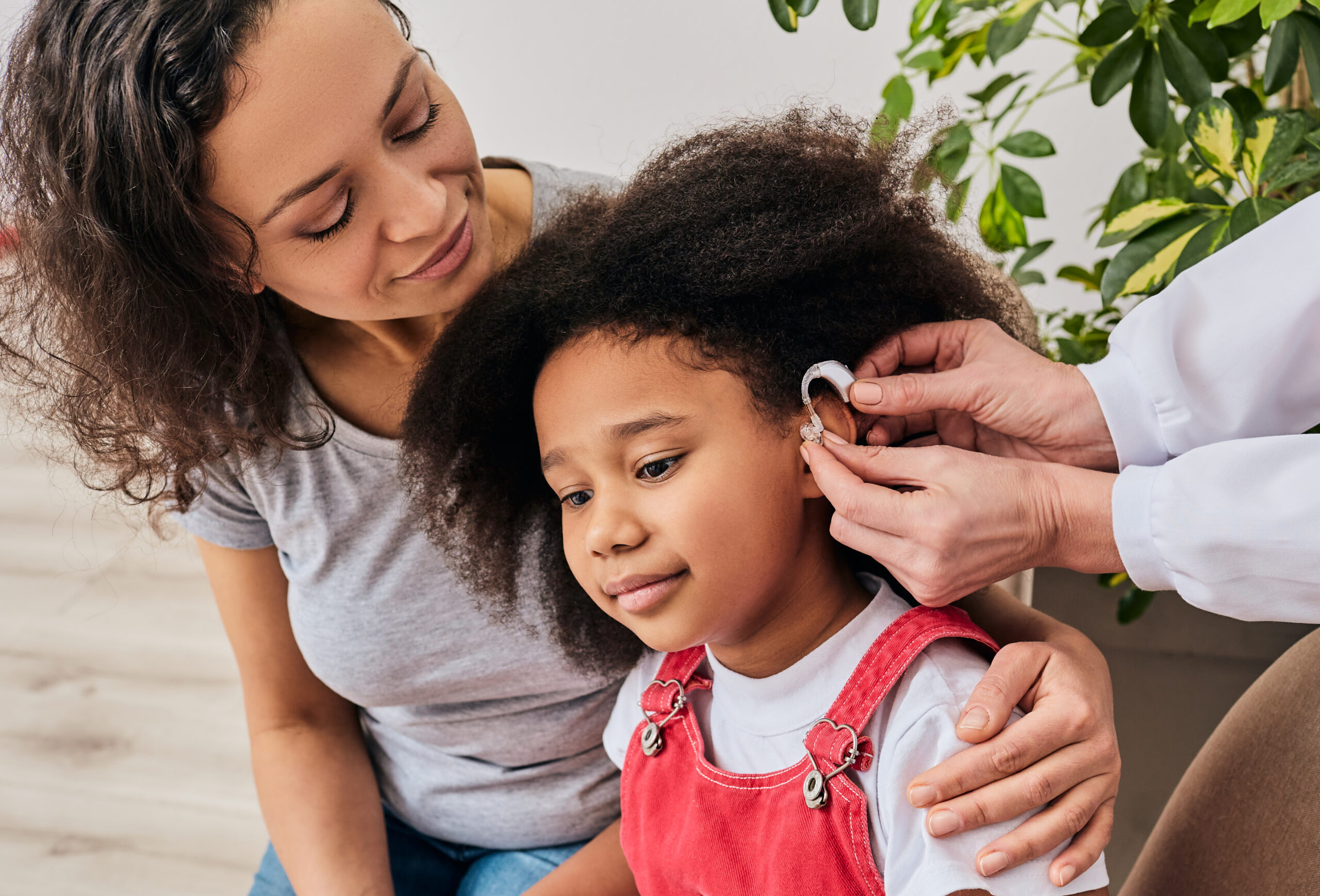 Hearing treatment for a child African American girl with her mother during installation hearing aid by her audiologist