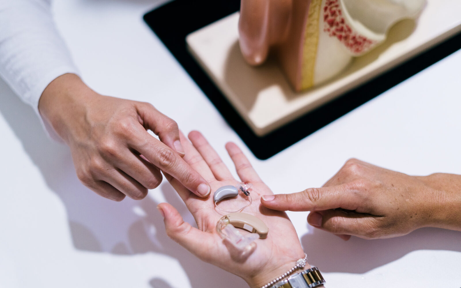 Close up Of Female Doctor Showing Hearing Aid To Patient In Clinic