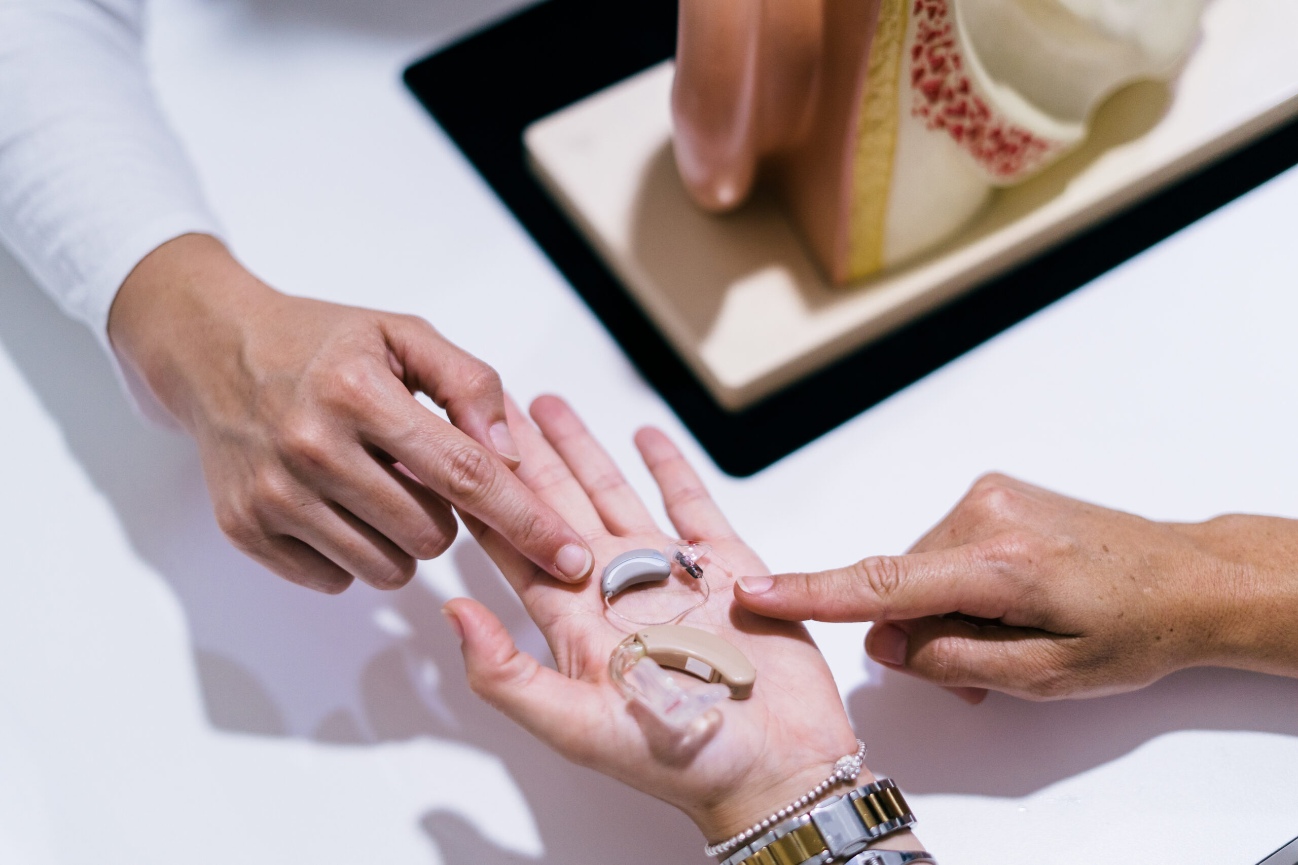 Close up Of Female Doctor Showing Hearing Aid To Patient In Clinic
