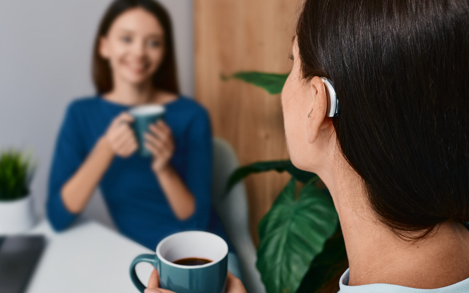 Adult woman with a hearing impairment uses a hearing aid to communicate with her female friend during tea drinking at home Hearing solutions