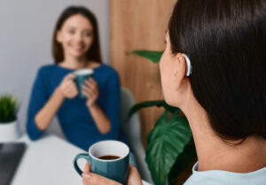 Adult woman with a hearing impairment uses a hearing aid to communicate with her female friend during tea drinking at home Hearing solutions