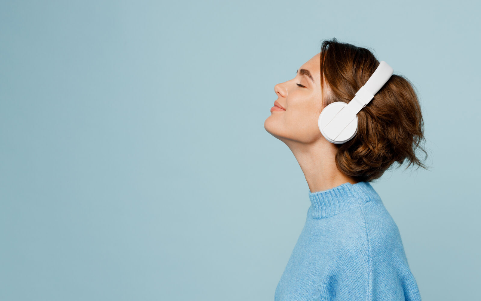 Young happy fun caucasian woman wear knitted sweater headphones listen to music with closed eyes have fun isolated on plain pastel light blue cyan background studio portrait People lifestyle concept