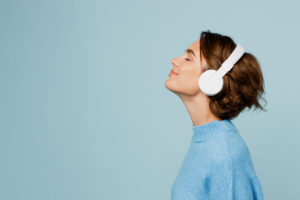 Young happy fun caucasian woman wear knitted sweater headphones listen to music with closed eyes have fun isolated on plain pastel light blue cyan background studio portrait People lifestyle concept