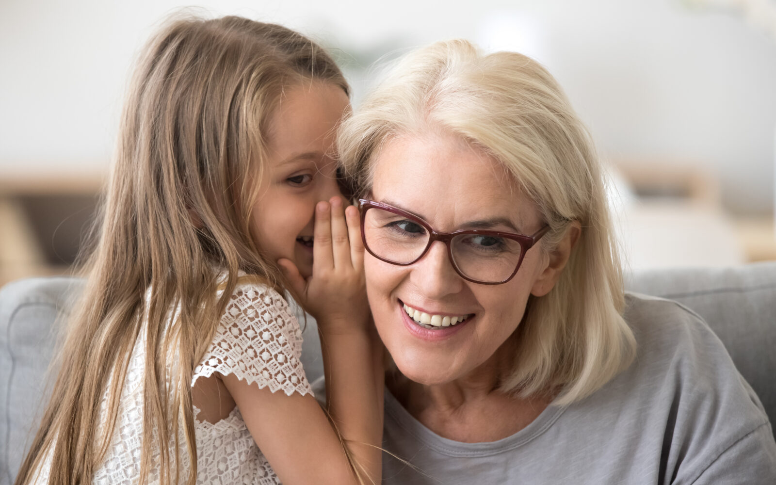 Cute little granddaughter whispering in ear telling secret to gr
