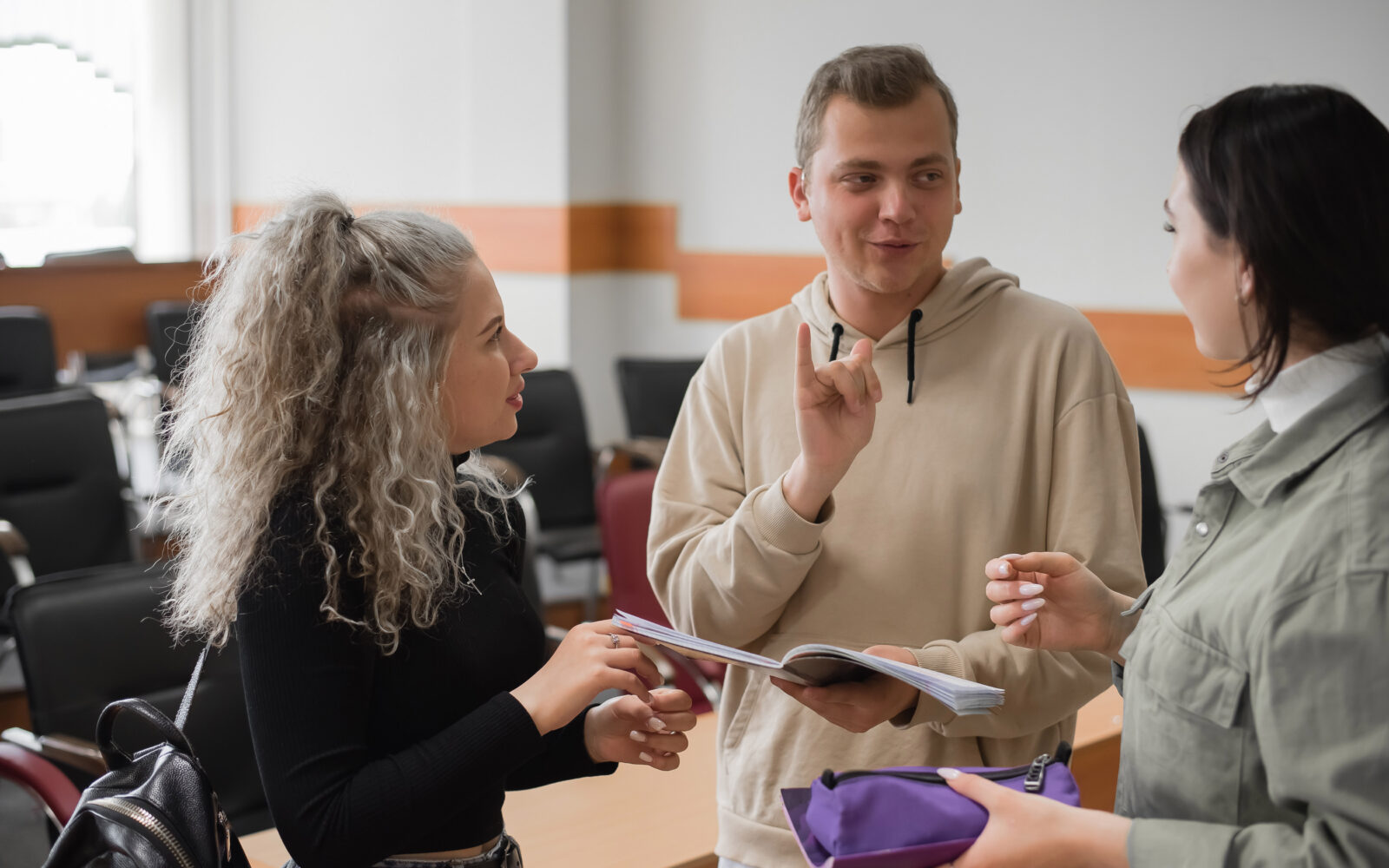 Two girls and a guy are talking in sign language Three deaf students chatting in a university classroom