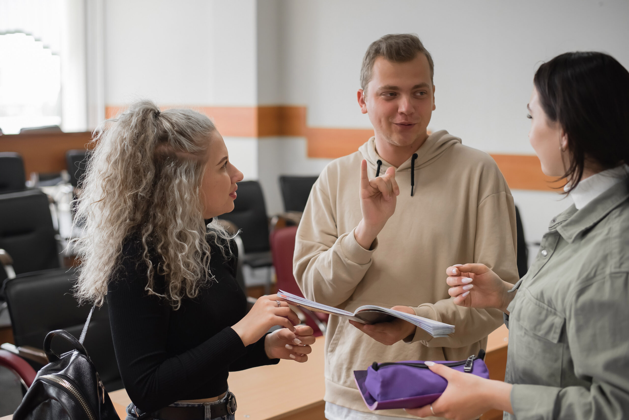 Two girls and a guy are talking in sign language Three deaf students chatting in a university classroom