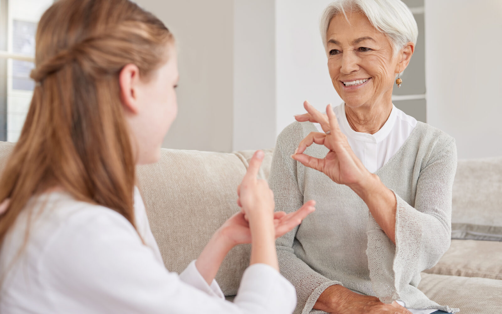 Senior woman, sign language and deaf girl communication, talking or conversation in home Support, care and retired old female speaking to child with hearing disability in asl language hand gestures