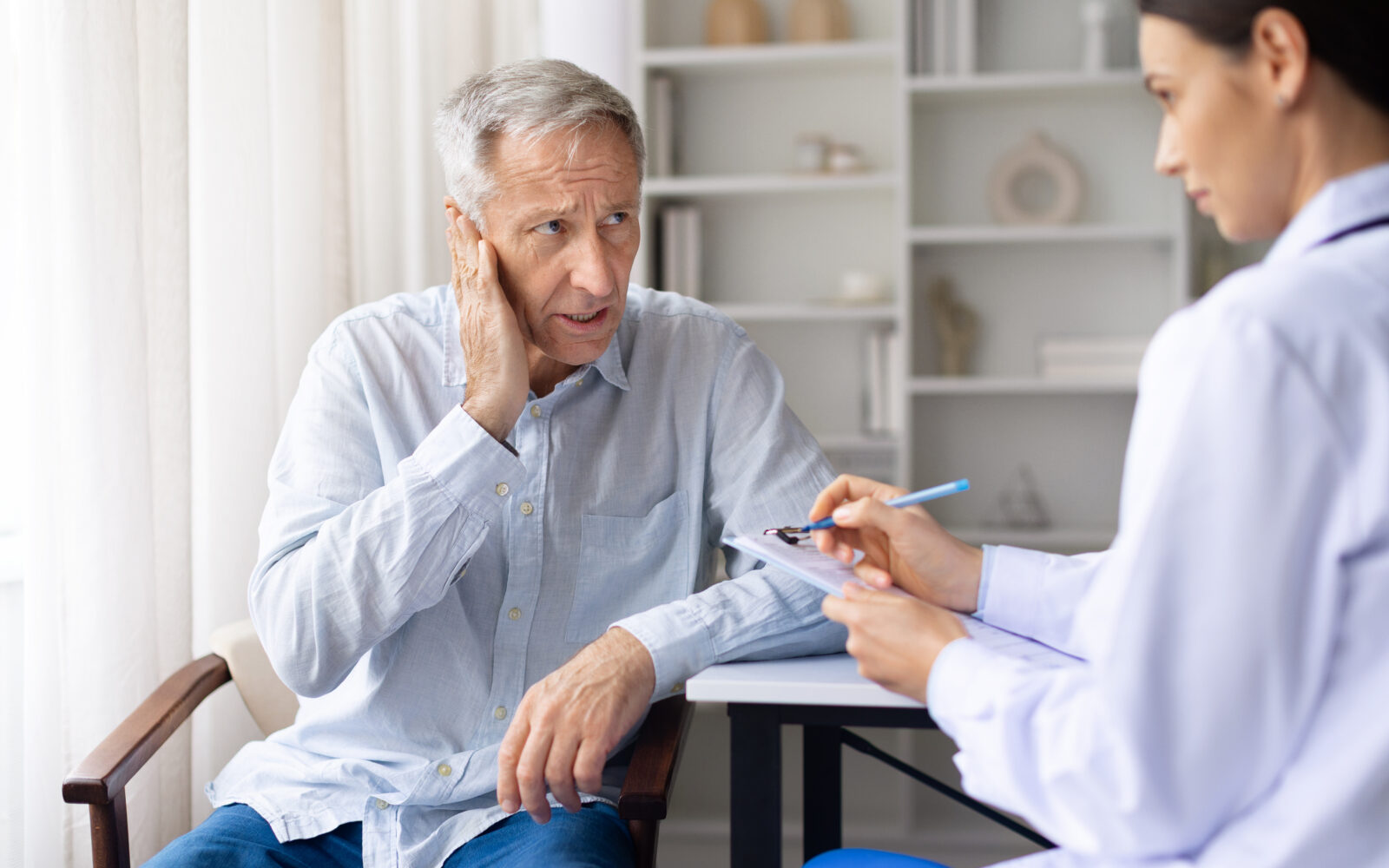 Senior male patient reporting ear pain to female doctor during medical visit