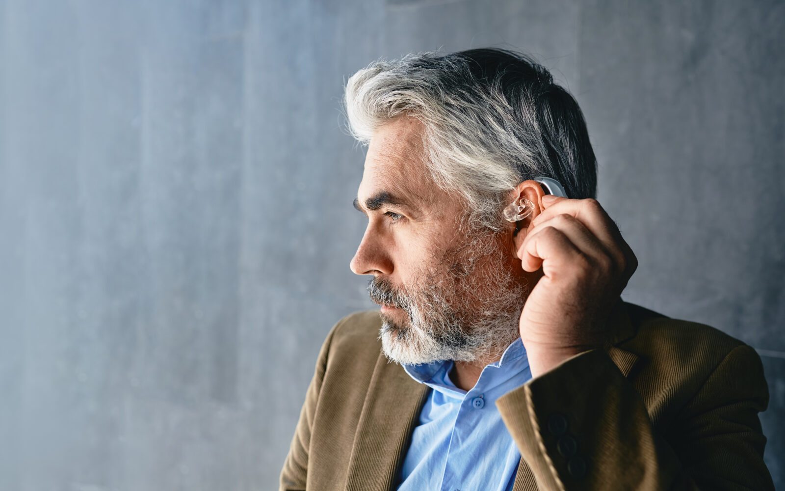 Grey haired mature man with hearing impairment using hearing aid Hearing solutions for deafness people