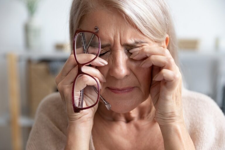 Close up of unhealthy elderly woman take off glasses massage eyes suffering from strong migraine or headache, unwell sick senior female grandmother struggle with blurry vision or dizziness at home