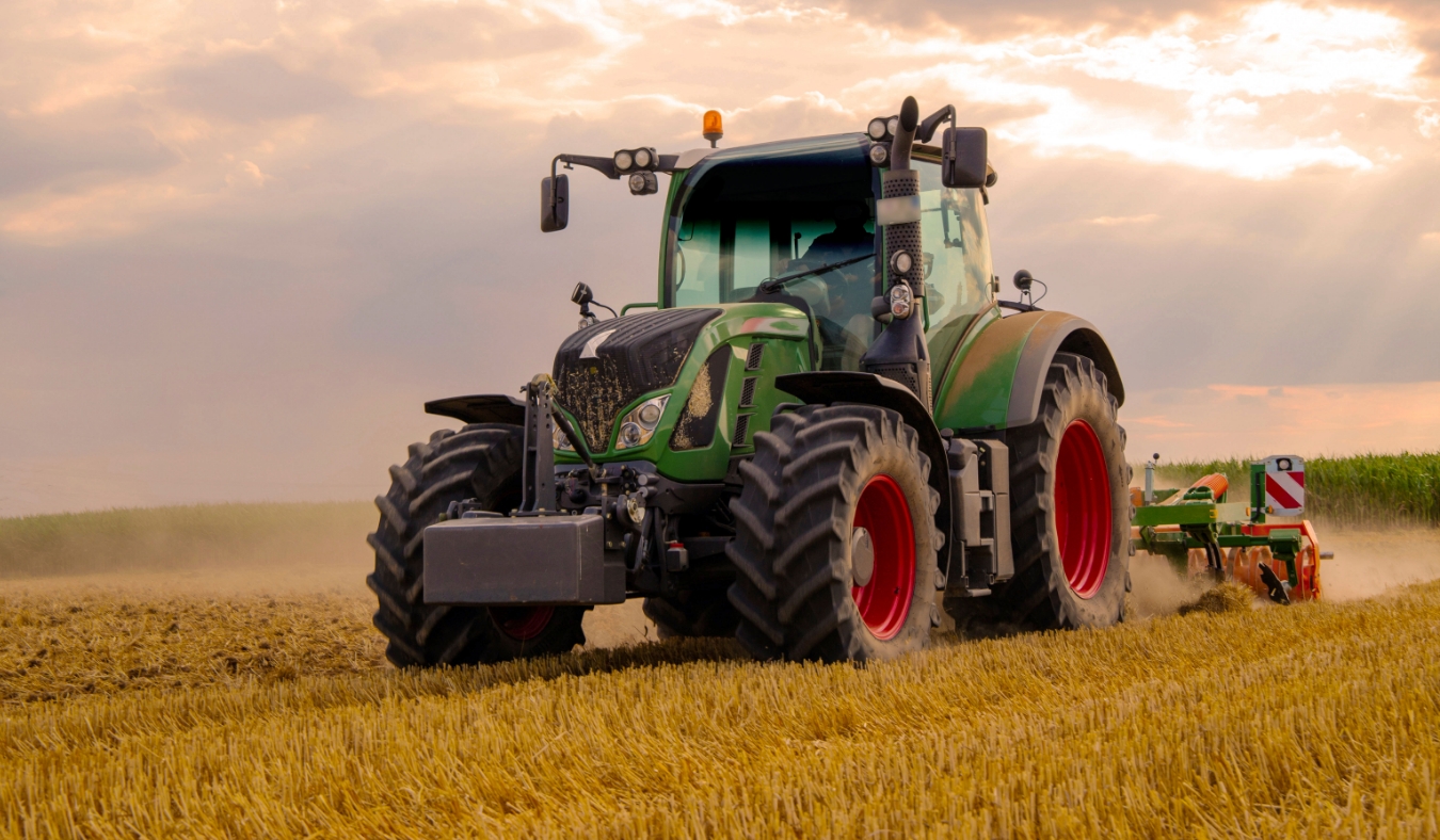 green tractor plowing cereal field with sky with clouds