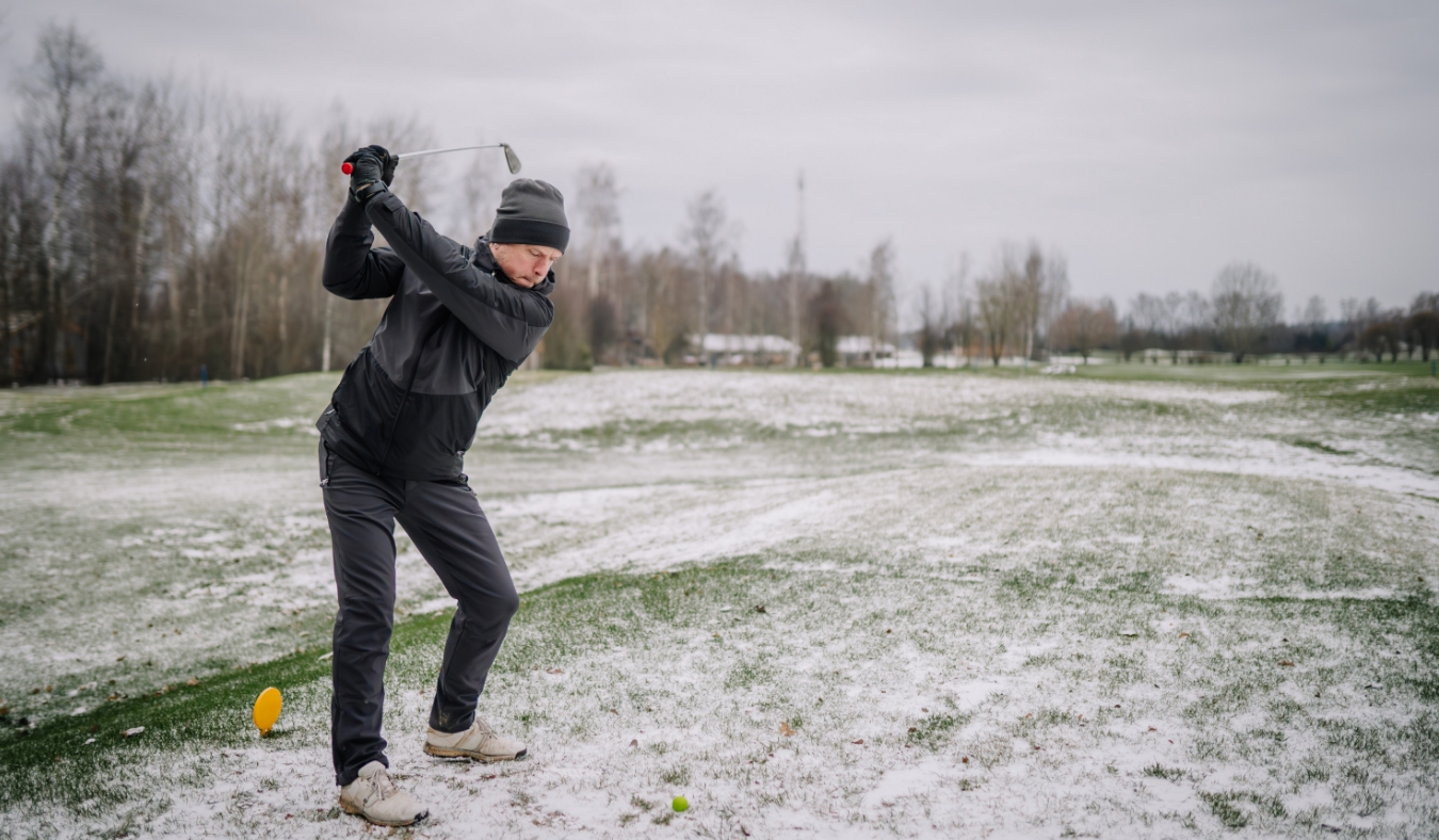 man makes a shot with a club on the golf course in winter