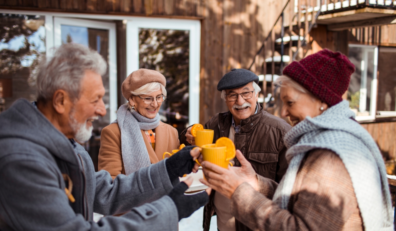 senior friends having hot drinks outside winter cabin