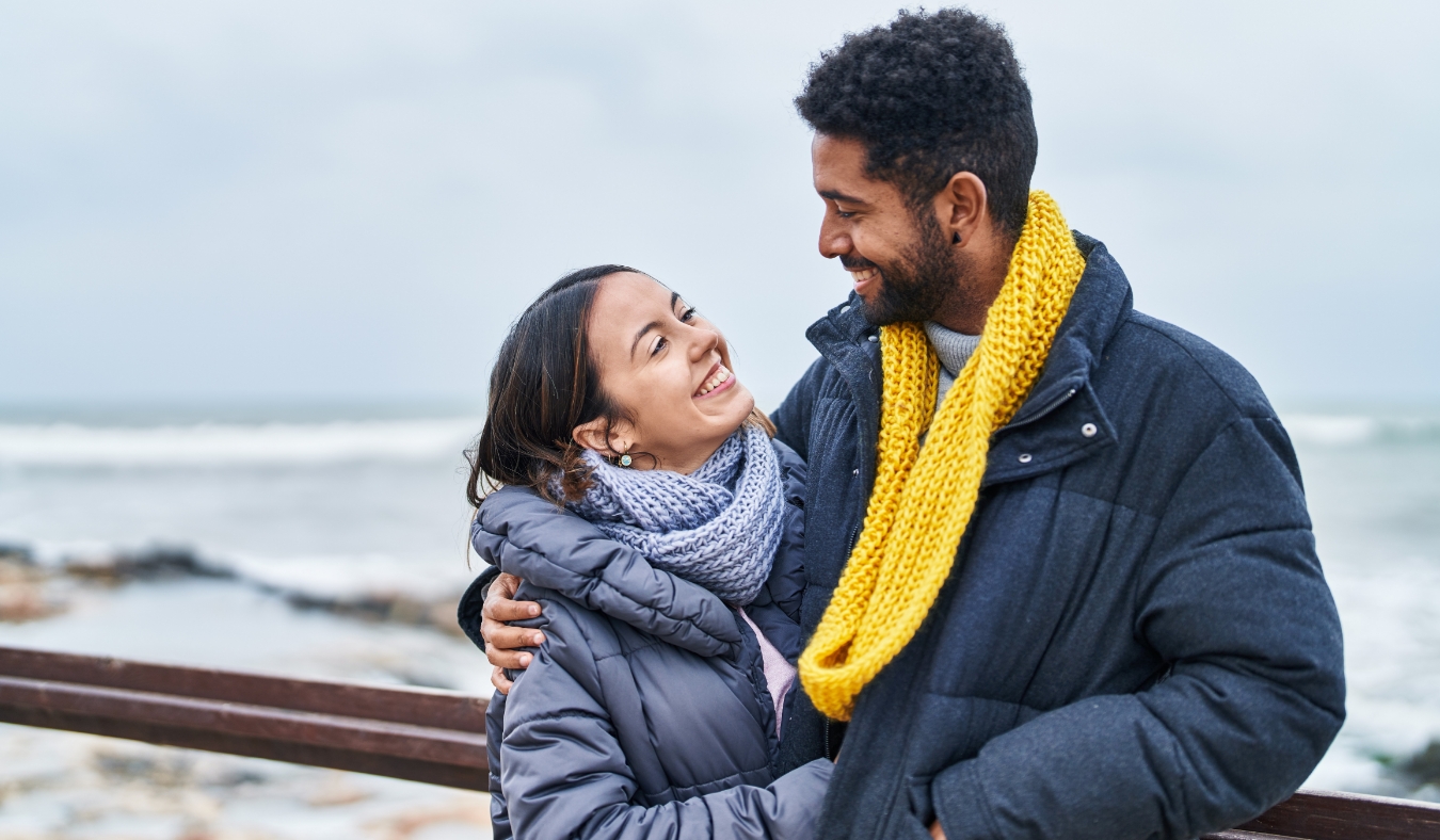 couple smiling confident hugging each other at chilly seaside