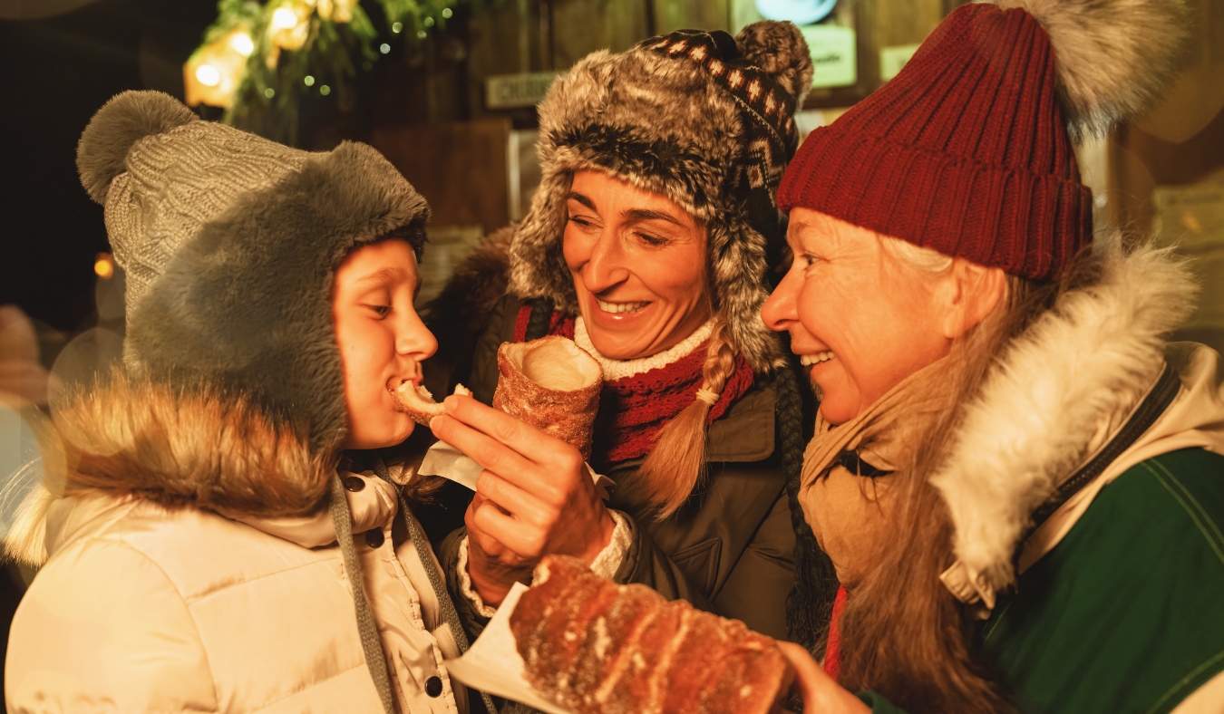 grandson eating pastry with grandmother and mother at holiday market