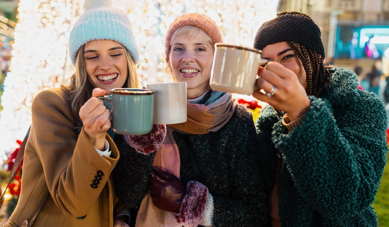 three friends enjoying hot drinks at holiday market