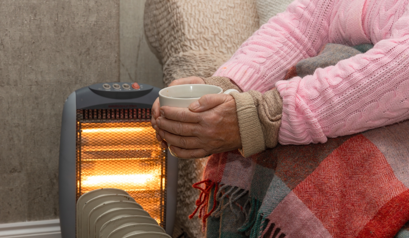 woman warming hands with hot coffe by heater