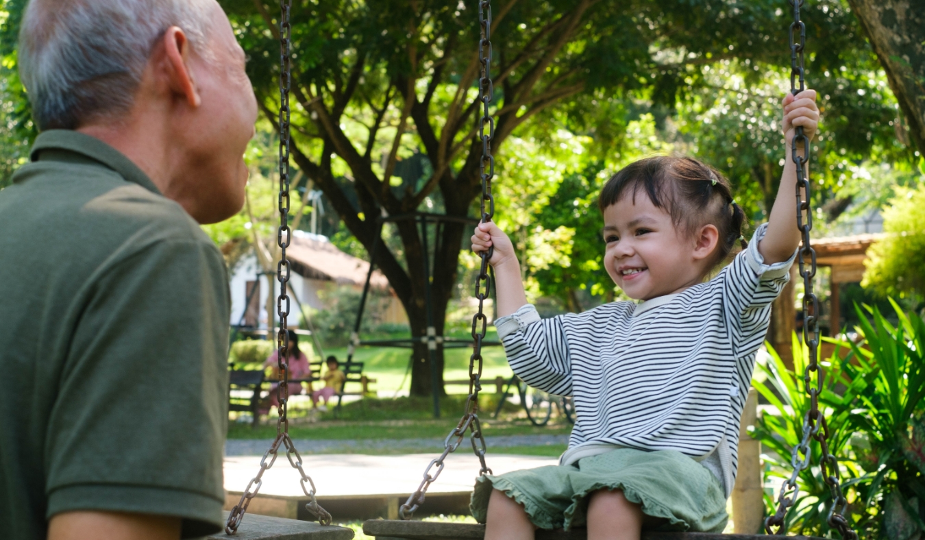 asian grandfather watching granddaughter swing outdoors