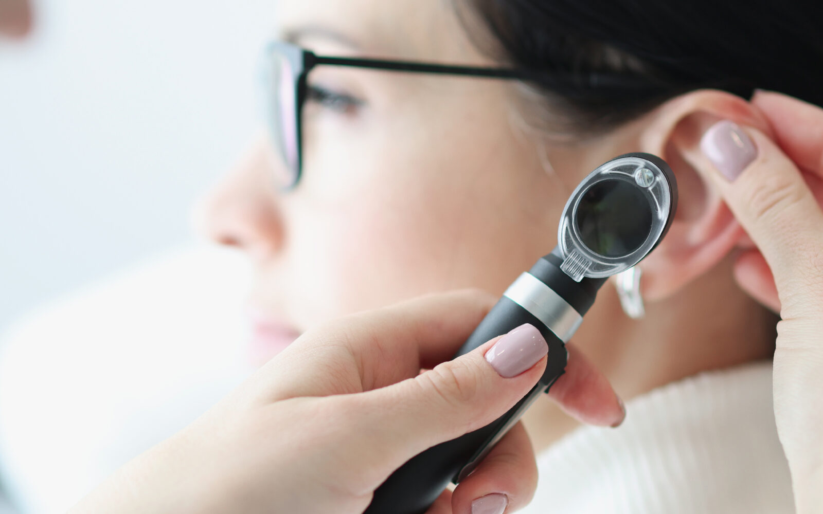 Otorhinolaryngologist examines patient ear with an otoscope