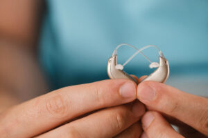 Hearing aids in hands making heart shape over blue background