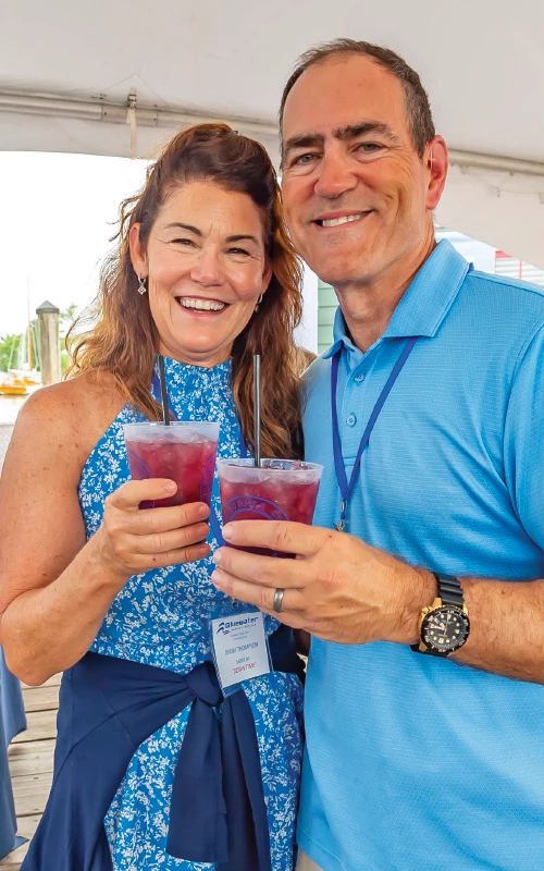 Smiling couple holding drinks at the Bluewater Summer Cruise welcome party in St. Michaels, Maryland