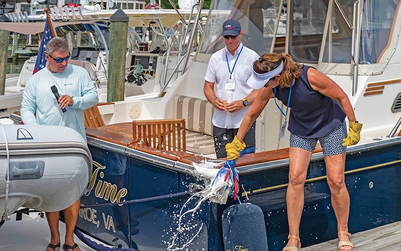 Woman breaking champagne bottle on yacht hull during boat christening at the Bluewater Summer Cruise