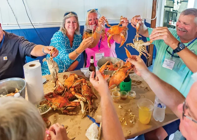 Group of guests raising steamed crabs and drinks during the Eastern Shore crab feast in St. Michaels