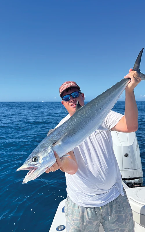 Angler proudly holding a freshly caught kingfish aboard the Valhalla V-33 with Mercury engines in the background