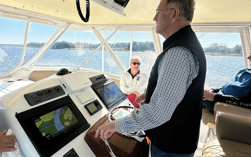 A man at the helm of an Ocean Yacht, steering while other passengers enjoy the enclosed bridge