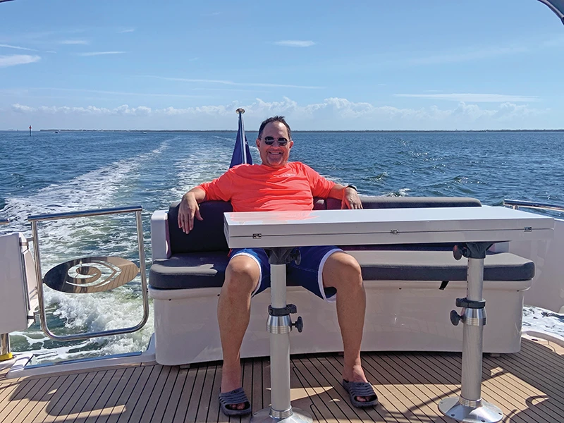 Kevin Boutin relaxes on the aft deck of his Elling E4 with a wide smile, cruising under clear blue skies.