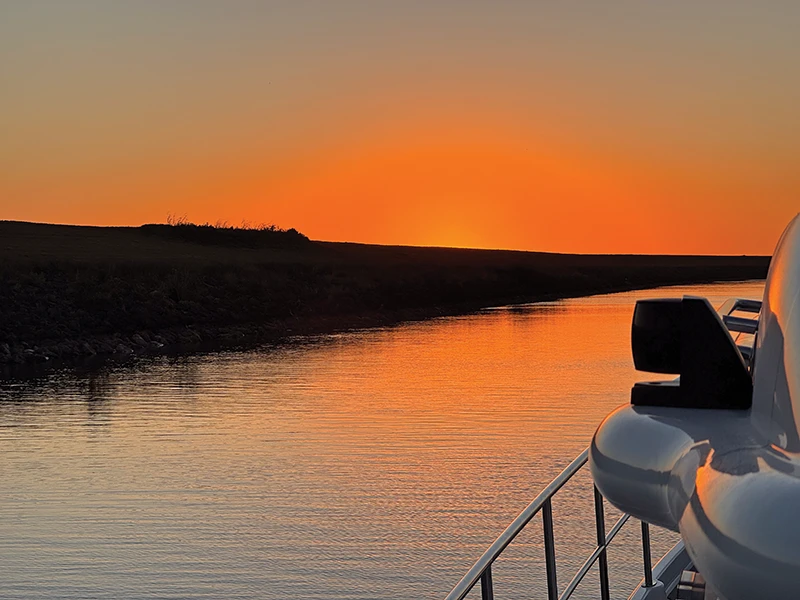 Golden sunset reflecting on calm inland waterway, viewed from the side deck of the Elling E4 during the 28-day journey