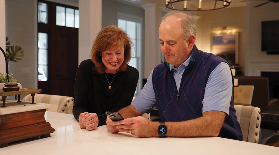 A couple smiling while reviewing information on a smartphone at home, illustrating remote access through the Sabre Connect app