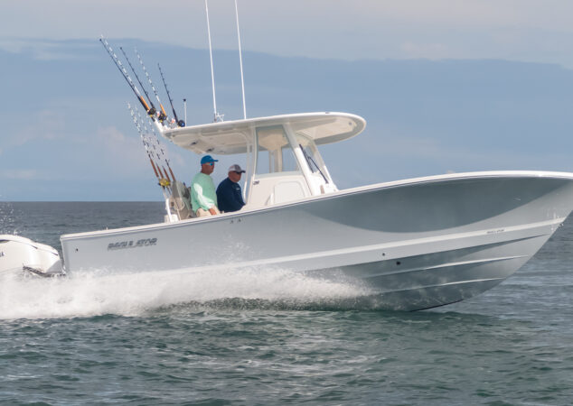 Regulator 28 center console cruising offshore with two passengers at the helm and fishing rods rigged on the hardtop