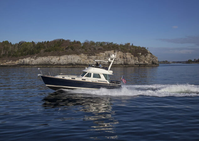 Sabre 48 Fly Bridge cruising offshore at speed, with rocky shoreline and trees in the background
