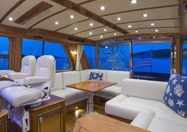 Salon with white leather seating, dual helm chairs, wood trim, and dining table, overlooking aft deck