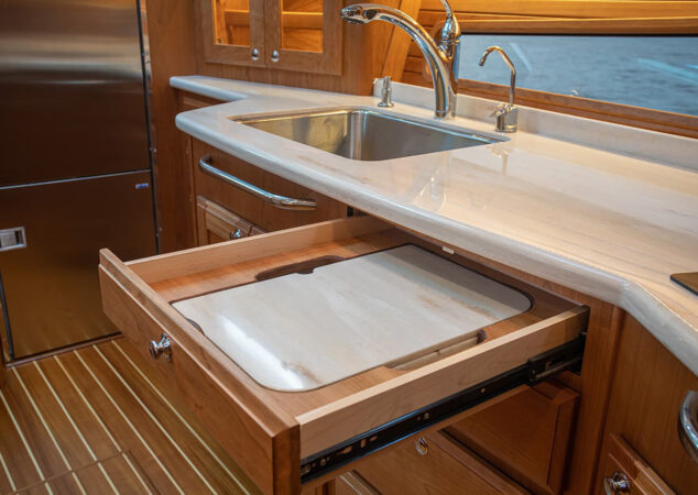 Galley detail showing pull-out cutting board drawer beneath solid-surface countertop and sink