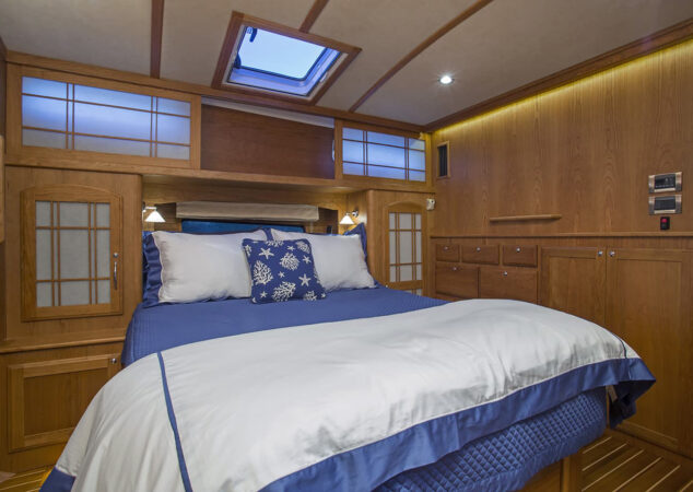 Master stateroom with island berth, blue bedding, and wood cabinetry featuring storage drawers