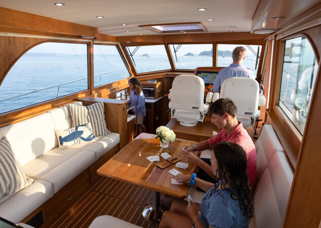 Salon interior with helm seats forward, family seated around table playing cards, and galley to port