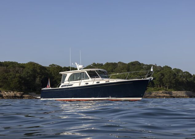 Back Cove 412 cruising offshore with navy hull and white cabin against a tree lined shoreline