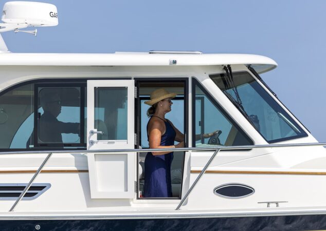 Helm of Back Cove 412 woman driving with sliding side door open and pilothouse windows visible