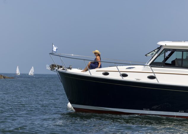 Woman sitting on bow of Back Cove 412 foredeck with sailboats in the distance