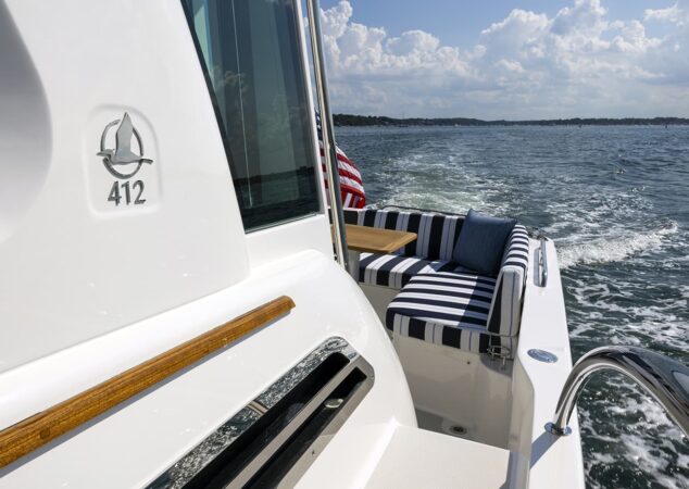 Back Cove 412 cockpit view showing striped lounge seating table and model badge with ocean backdrop