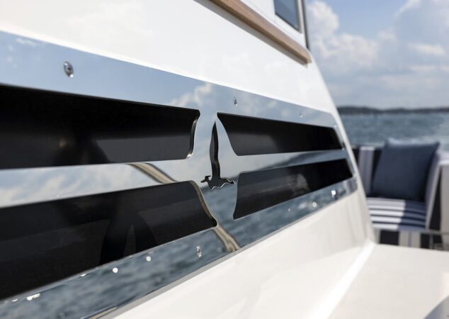 Back Cove 412 transom detail featuring polished chrome bird logo with striped cockpit seating in background